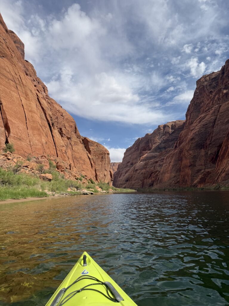 A green kayak on the Colorado river with calm waters and tall mountain walls  on both sides of the river. 
