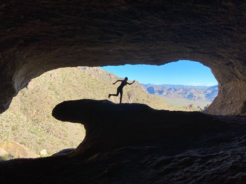 Inside of cave shaped like a wave and a woman pretending to surf the wave. 