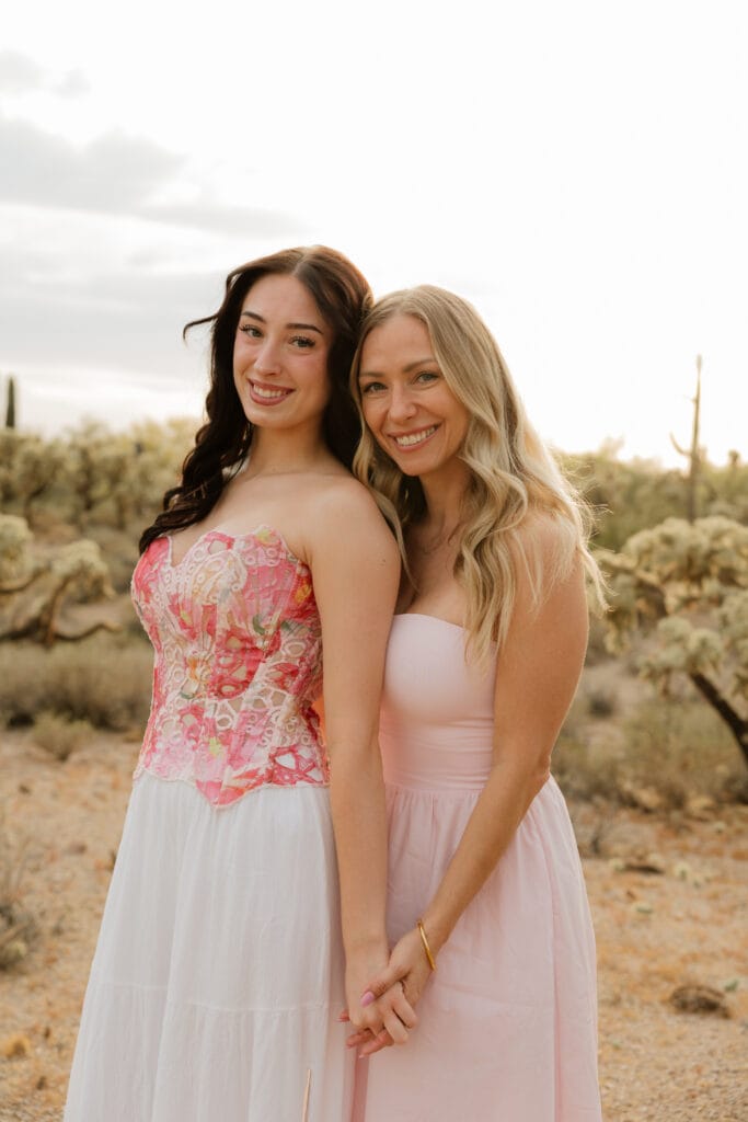 A brunette woman on the left and blonde woman on the right standing next to each other in the desert holding hands. 